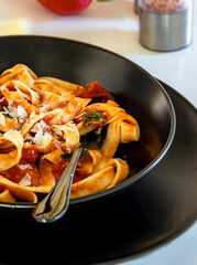 Italian lunch. Neapolitan pasta. Italian pasta dish with tomatoes, basil, onions. Black plate.