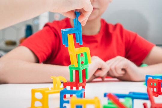 Cropped photo of preteen children sitting at white table, playing board game stacking chairs, putting colorful plastic small chairs in stack for building balancing tower. Board games, entertainment.
