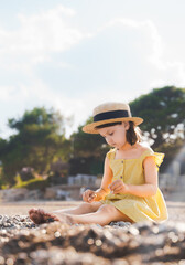 Little girl walking on beach, sea ocean shore in romantic yellow dress, straw hat. Playing in sand, blue waves. Family vacation travel leisure in hot summer coast. Sunny day relax in hotel resort