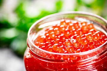 An open jar of red caviar with greens.