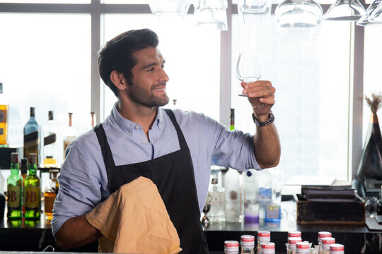 Young caucasian man is bartender cleaning and wipe glass with professional at counter, portrait handsome male preparation glass or wineglass, barman standing with confident at restaurant luxury. - Powered by Adobe