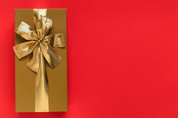 Golden gift box with golden ribbon and bow on a red background. Top view. Copy space.