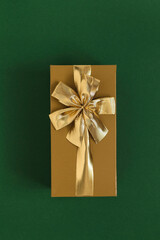 Golden gift box with golden ribbon and bow on a green background. Top view. Copy space.