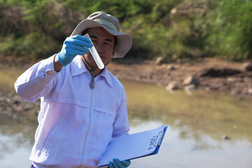 Asian man environment researcher holds tube of sample water to inspect at the lake. Concept,...
