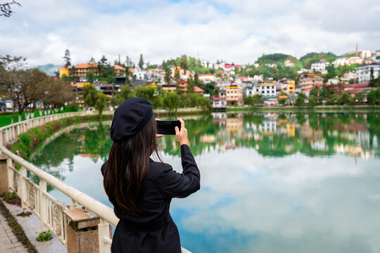 Young woman taking a photo at Sapa lake with reflection and blue sky in Lao Cai province, Vietnam