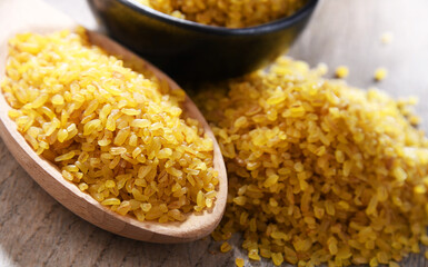 Composition with a bowl and spoon of uncooked bulgur on a table