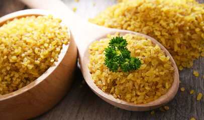 Composition with a bowl and spoon of uncooked bulgur on a table