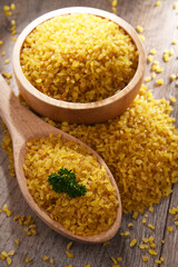 Composition with a bowl and spoon of uncooked bulgur on a table