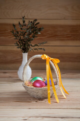 Easter basket filled with hand painted pastel Easter Eggs over white background. Next to vase with eucalyptus leaves.