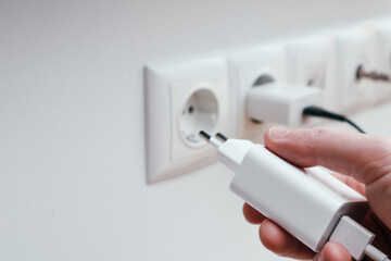 Man hands plugging the charger into an outlet in the wall, close-up. Hand turns on, turns off...