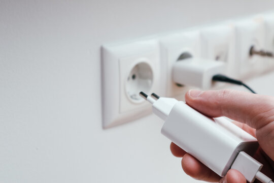Man hands plugging the charger into an outlet in the wall, close-up. Hand turns on, turns off charger in electrical outlet on wall