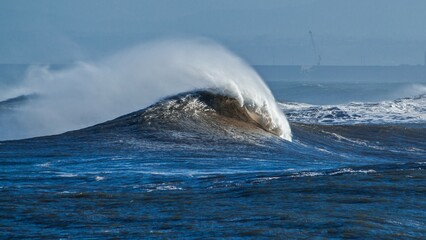 Big blue wave with a big wakeand a tube inside breaking in the middle of the ocean with mist at day