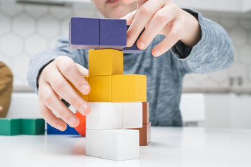 Cropped photo of preteen children friends sitting at table, building tower of colorful toy wooden construction blocks.