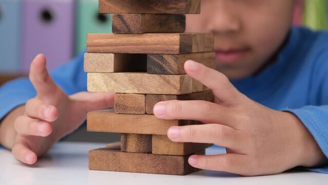 Cute little girl playing with wooden game (jenga) on a table in a room at home. Asian child playing wood blocks stack game indoors. Learning and development of fine motor skills.