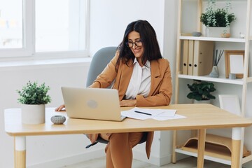 Business woman working in the office at her desk with a laptop, smile and business dialogue via...