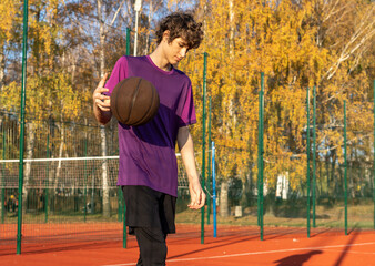 Cute young teenager in t shirt with a ball plays basketball on court. Teenager running in the stadium. Sports, hobby, active lifestyle for boys