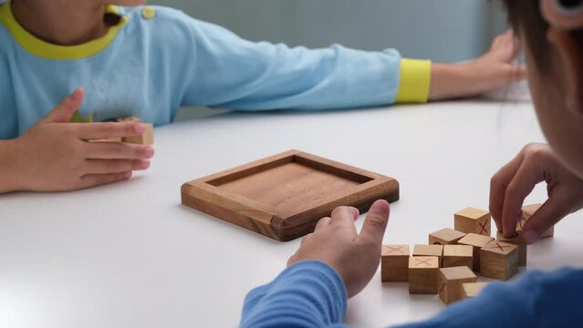 Little siblings playing wooden board game tic-tac-toe on table in living room. Family spending time together on weekend.