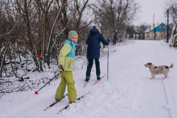 Happy child is skiing in the park. A teenager is engaged in winter sports in nature with his beloved pet. A beautiful girl walks with a dog along a winter road. Children go skiing during the holidays.