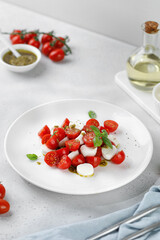 Caprese Salad with ripe tomatoes, mozzarella cheese, fresh basil, balsamic sauce, pesto on white plate. Healthy delicious diet salad.