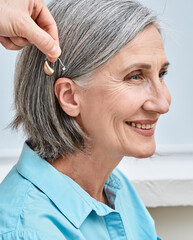 Doctor audiologist applying hearing aid to senior woman's ear. Hearing-impaired woman needs hearing...
