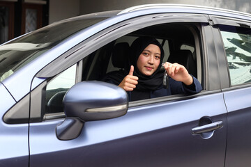Fototapeta na wymiar Muslim woman in hijab driving and showing car keys out the window while giving the thumb up.