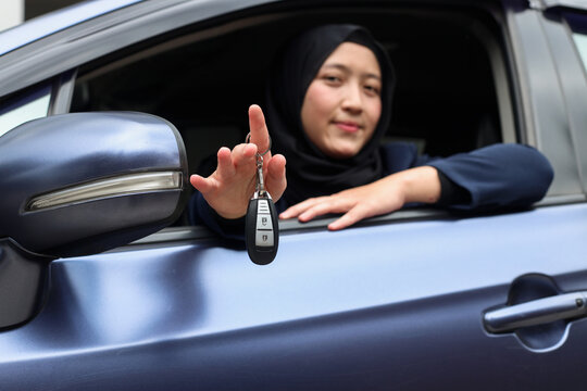 Muslim woman in hijab driving and showing car keys out the window