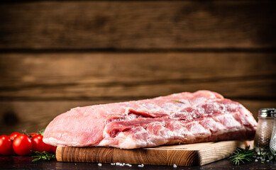 Raw pork on a cutting board with fresh tomatoes. 