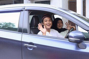 Muslim couple are smiling and waving hand inside the car ready to go on holiday. Mudik lebaran at Eid moment. 