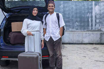 Muslim couple wearing white muslim wear is bring backpack and luggage in the back of car, ready to go on holiday. Eid moment background with copy space. 