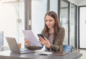 Fototapeta premium Marketing, Finance, Accounting, Planning, Businesswoman of bi nationality is talking with a customer representing a company distributor using a smartphone with laptop pen and notepad on office desk.