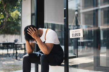 Young asian male coffee shop owner feeling stress or depress while sitting in front of his coffee shop.