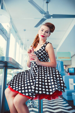 Retro (vintage) portrait of pretty smiling young woman sitting in cafe. Pin up style portrait of young girl in dress