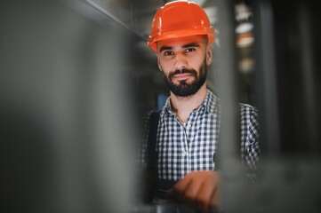 Portrait of Professional Heavy Industry Engineer Worker Wearing Safety Uniform, Hard Hat Smiling. In the Background Unfocused Large Industrial Factory.