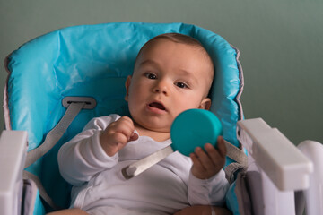 Obraz premium baby in the child chair playing with kitchen utensil