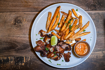 Grilled pork steak served with french fries, sliced lime, and chili sauce on the white plate. Bokeh...