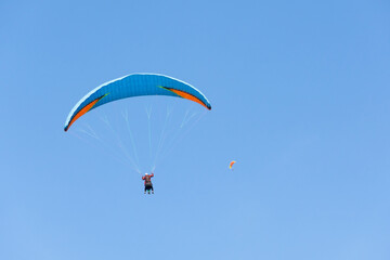 Fototapeta na wymiar Two paraglider tandem fly against the blue sky, tandem paragliding on distance guided by a pilot.