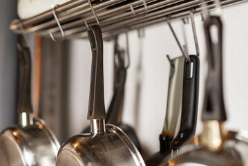 Frying pans and kitchen utensils hang on hooks in the kitchen. Storage of cooking utensils.