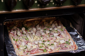 Cooking homemade pizza on a baking sheet in the oven. Pizza with mozzarella cheese, herbs and ham.