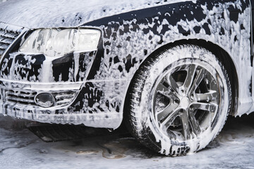 the car at the car wash is covered with foam, wash under pressure with a stream of water