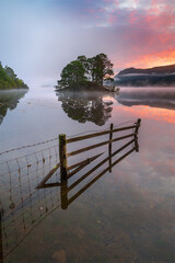Derwentwater Sunrise, Lake District, UK. A flooded wooden fence leading into misty view of colourful sky, reflecting in the water.  - 563628920