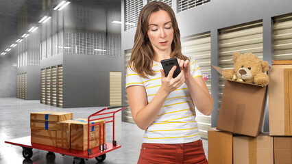 Woman in hallway of storage company. Girl with phone near boxes. Woman rents storage room. Storage Units for storing personal items. Cart with box behind girl. Warehouse space behind lady