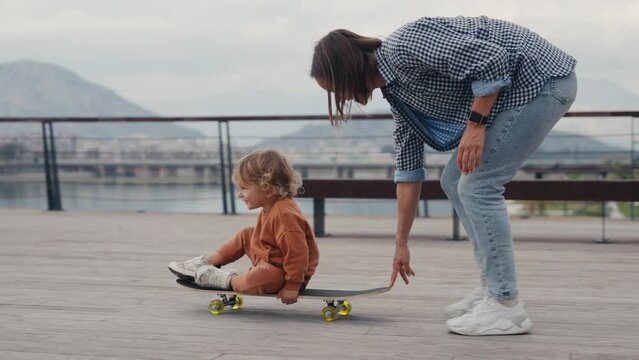 Mother pushing little son sitting on skateboard. High quality 4k footage