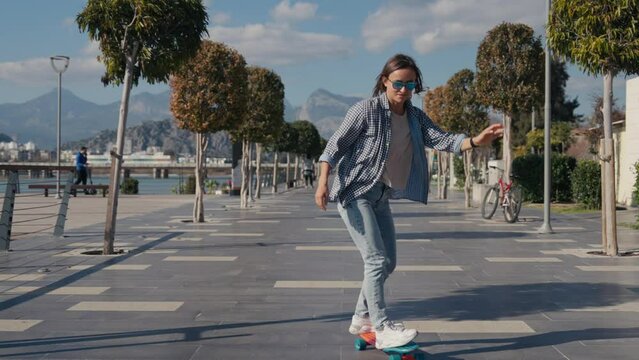 Young stylish teenage girl learning to ride skateboard. Trendy girl first time tries to ride skateboard. High quality 4k footage