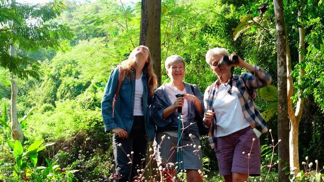 Teenager girl and two grandmother traveling travel to forest and adventure while using binoculars exploration together with happy, senior woman and granddaughter hiking with fun and vitality.