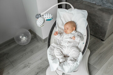 Adorable baby sleeps in baby rocker in room. Newborn concept.