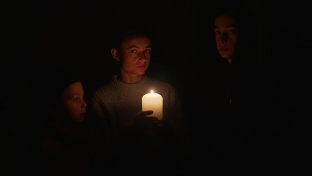 Woman with two children waiting at home by the candles during the blackout. Mother with her sons under candle lights during a balckout due to energy crisis in Ukraine.