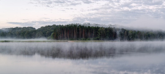 Mystical landscape. Rivers with a strip of forest in the fog at dawn.