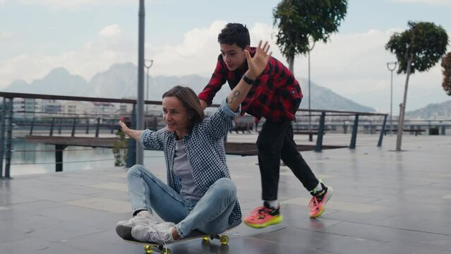 Cheerful son pushing his mother on a skateboard and laughing. Wild and crazy