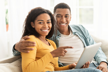 Happy young african american guy and lady point finger at phone, have video call, surfing in internet