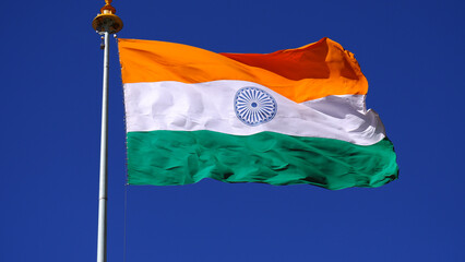 Indian national flag hoisting high under blue sky.